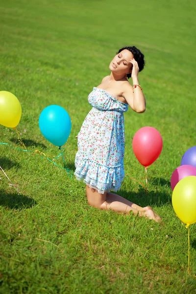 Pregnant woman with balloons on grass — Stock Photo, Image