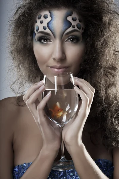 Chica con maquillaje, con un pez en un vaso en la mano — Foto de Stock