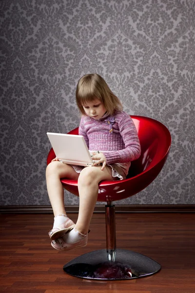 Flickan sitter i en stol med en bärbar dator — Stockfoto