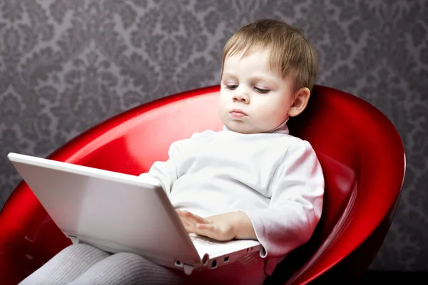 Pojken som sitter i en stol med en bärbar dator — Stockfoto