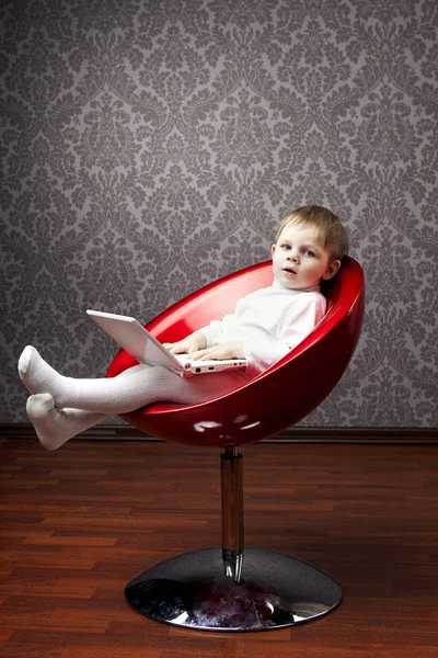 Niño sentado en una silla con un ordenador portátil — Foto de Stock