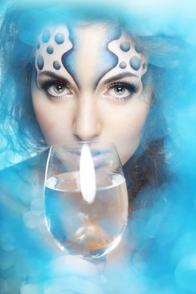 Dziewczyna z makijażem, z rybą w szklance w dłoni — Zdjęcie stockowe