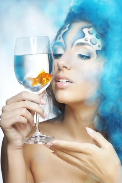 Meisje met make-up, met een vis in een glas in haar hand — Stockfoto