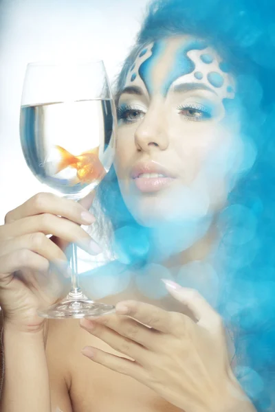Ragazza con il trucco, con un pesce in un bicchiere in mano — Foto Stock