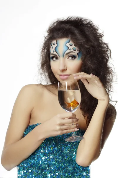 Meisje met make-up, met een vis in een glas in haar hand — Stockfoto