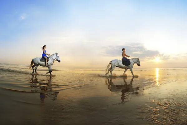 Verliebtes Paar, das auf einem Pferd des Meeres bei Sonnen galoppiert Stockbild