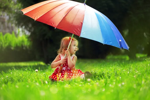 Kleines Mädchen mit Regenbogenschirm im Park Stockbild