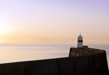 Lighthouse at the end of a breakwater wall during sunrise clipart