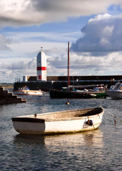Маленькая лодка, связанная в гавани с маяком — стоковое фото