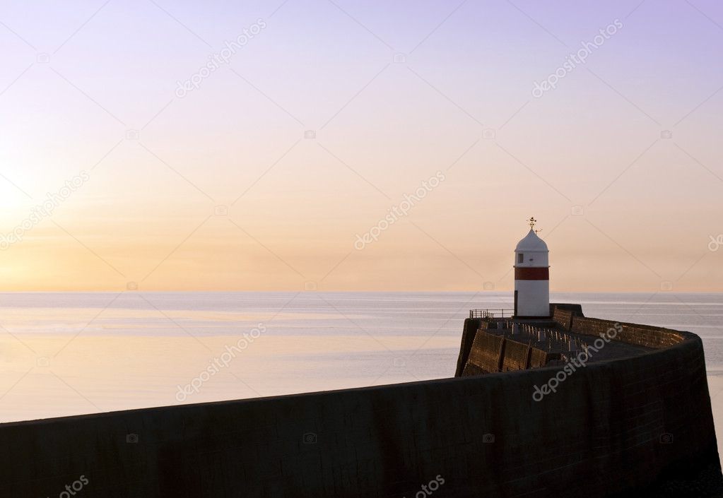 Lighthouse at the end of a breakwater wall during sunrise
