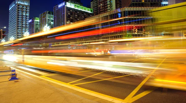Sentiers lumineux de bus à grande vitesse et flous dans le paysage nocturne du centre-ville — Photo