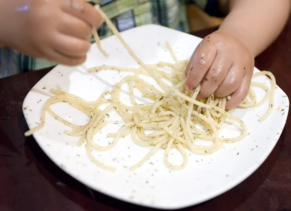 Еда ребенка, чтобы захватить макароны с руки — стоковое фото