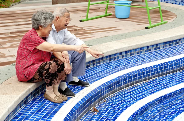 A senior couple sitting beside a pool — Stock Photo, Image