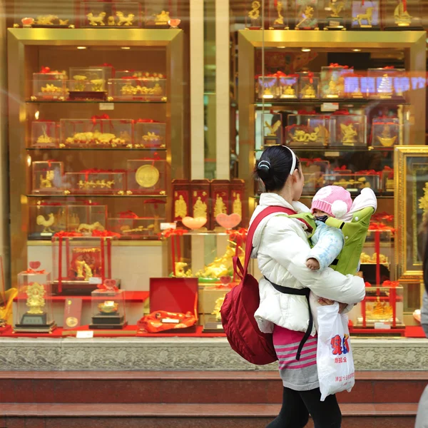 Matka drží dítě Hledat v okně zlaté shop — Stock fotografie