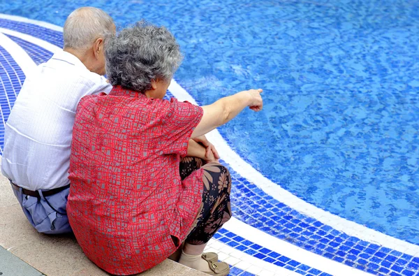 Una íntima pareja de ancianos sentados al lado de una piscina — Foto de Stock