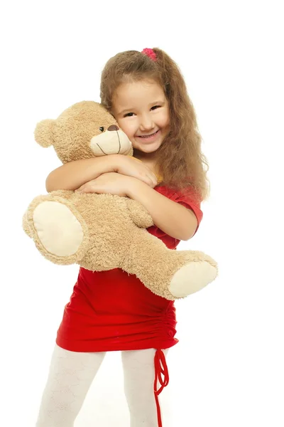 Den lille smilende jenta klemmer med bjørn i rød kjole – stockfoto