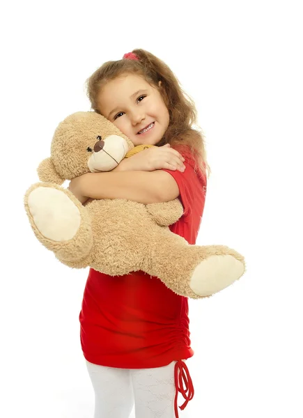 Маленькая улыбающаяся девочка обнимается с медведем в красном платье — стоковое фото
