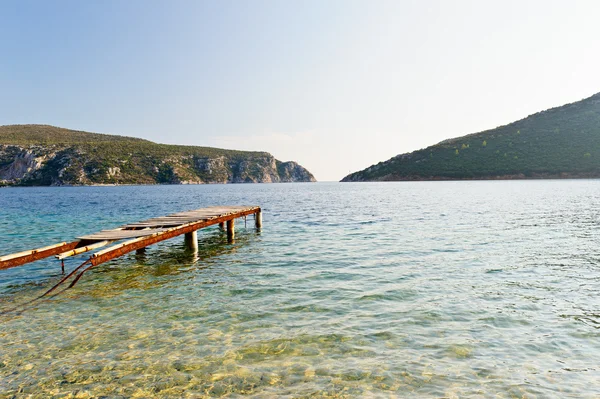 Old pier in rocky bay with awesome transparent water — Stock Photo, Image