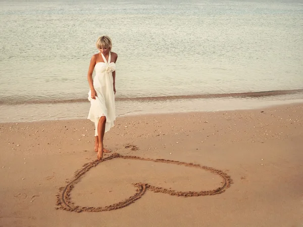 Dziewczyna zwraca się serce w piasku — Zdjęcie stockowe
