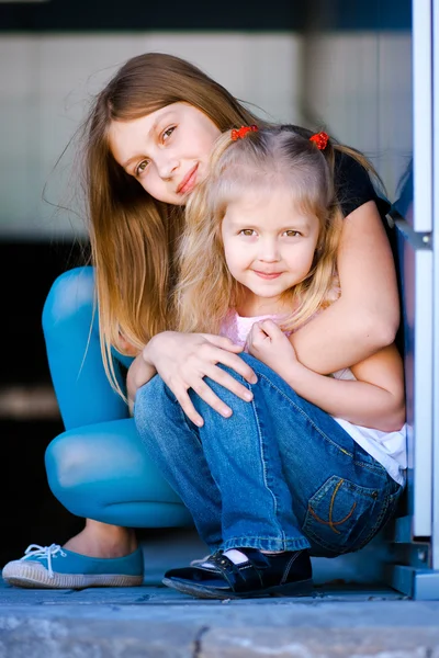 Twee kleine meisjes zitten knuffelen en glimlachen — Stockfoto