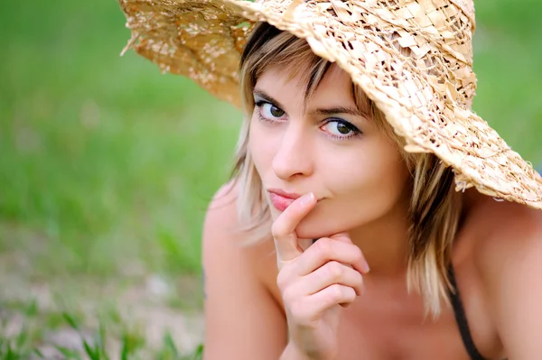 Mooi meisje liggen op het gras in een stro hoed — Stockfoto