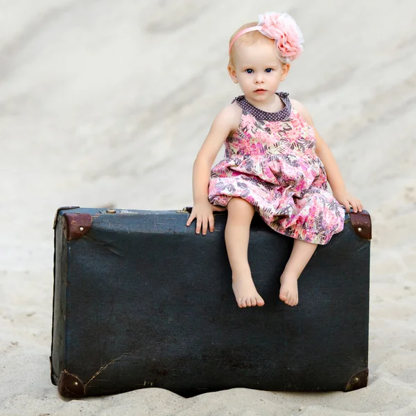 Kleines Mädchen sitzt auf einem Koffer in der Wüste — Stockfoto