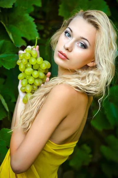 Schöne blonde Mädchen in grünen Weintrauben — Stockfoto