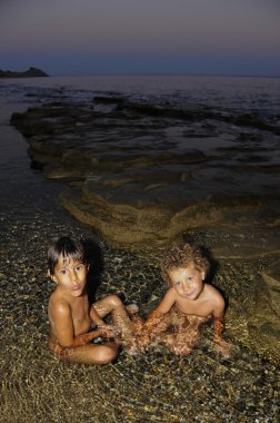 Two little girls playing in water at seaside at dusk