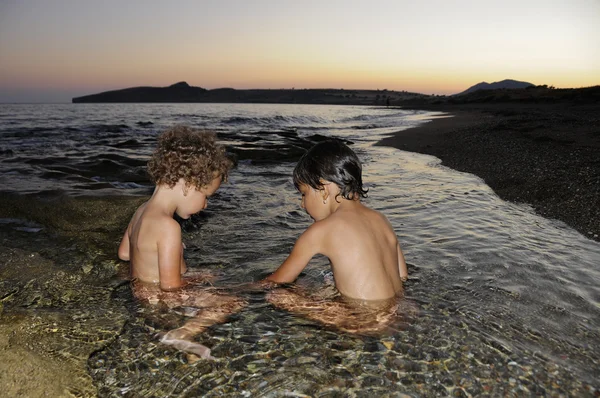 Dvě malé holčičky hrají ve vodě u moře za soumraku — Stock fotografie