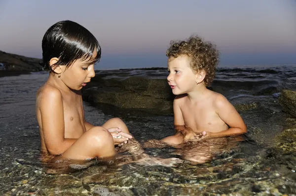Дві маленькі дівчата грають у воді біля моря в сутінках Стокова Картинка
