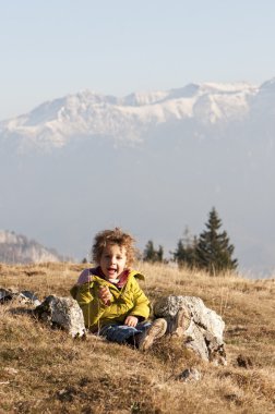 Happy toddler girl on meadow with snow capped mountains background clipart