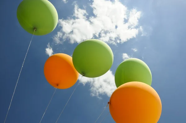 Gröna och orange ballonger flyger mot solen Royaltyfria Stockfoton