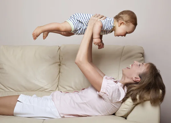 Bebé y madre jugando / volando en el sofá —  Fotos de Stock