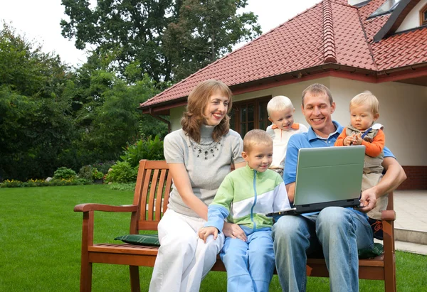 Familie schaut Laptop auf der Bank vor dem Haus Stockfoto