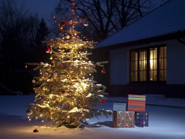Kerstboom met huis buiten met geschenkdozen Stockfoto