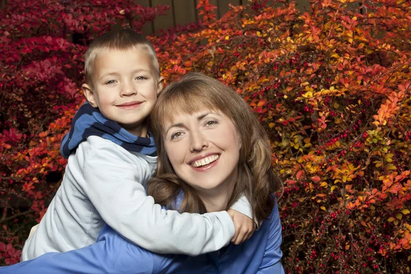 Mother and son piggyback on Fall background — Stock Photo, Image