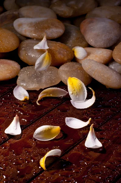 Yellow flower petals with yellow river stone on wood — Stock Photo, Image