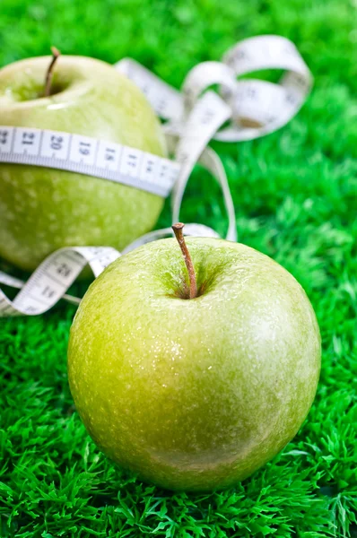 Två äpplen på gräset och en med ett måttband — Stockfoto