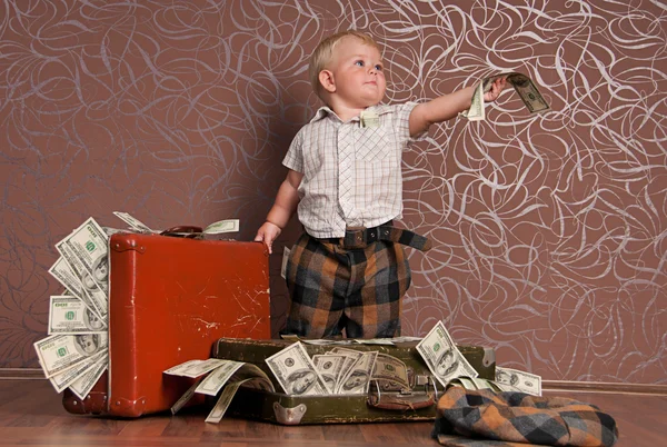 A little boy stands next to the suitcases full of money and handed a bill o — Stock Photo, Image
