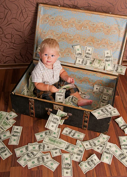The boy is sitting in a suitcase with the money and keeps dollars — Stock Photo, Image