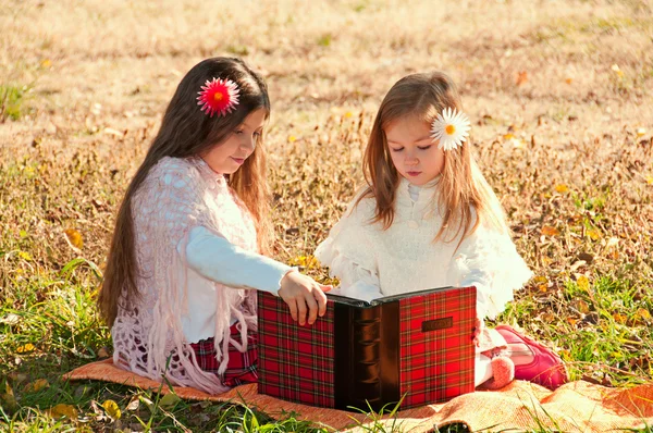 Duas meninas lêem o livro enquanto estão sentadas na grama . — Fotografia de Stock