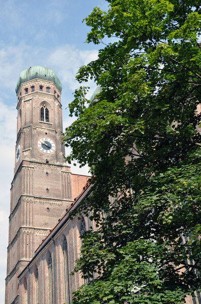 One of the mighty towers of Frauenkirche cathedral, partially hidden behind a tree.