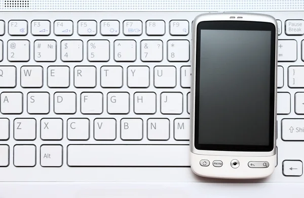 Teléfono inteligente sobre teclado blanco — Foto de Stock
