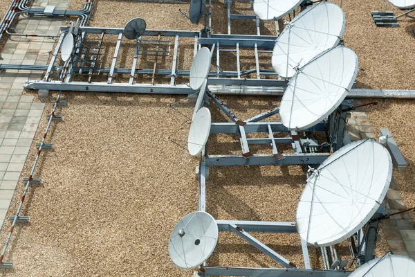 Коллекция больших спутниковых тарелок на плоской гравийной крыше — стоковое фото