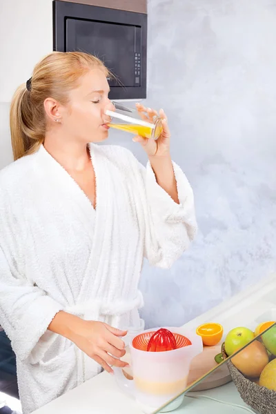 Ung kvinna dricker färsk juice i kök — Stockfoto