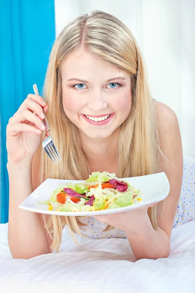 Woman eating salad in bed — Stock Photo, Image