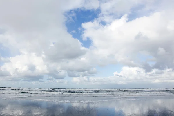 Wolken en blauwe hemel weerspiegeld in natte strand — Stockfoto