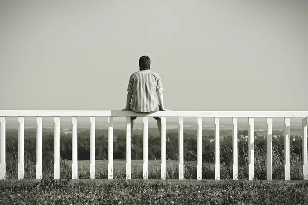 Человек, сидящий на заборе с видом на пейзаж — стоковое фото