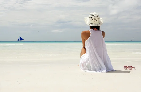 Chica en un sombrero sentado en la playa y mirando en el horizonte —  Fotos de Stock