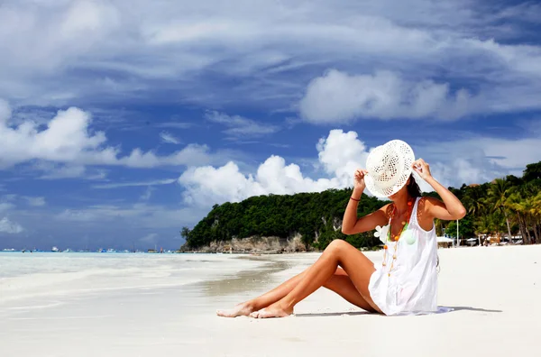 Привлекательная девушка в шляпе сидит на песке тропического пляжа — стоковое фото